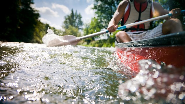 Mann padelt mit Kanu auf dem Wasser.