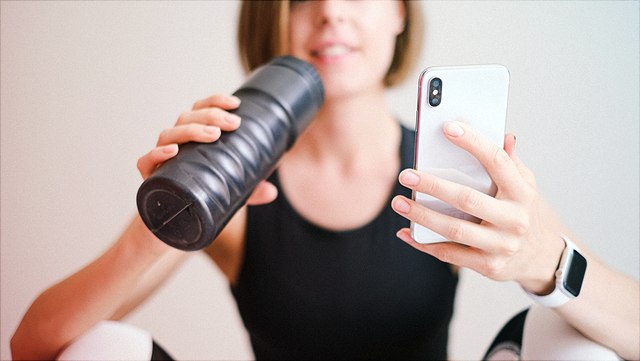 Junge Frau hält Trinkflasche in der einen und Handy in der anderen Hand.